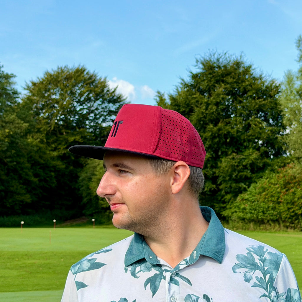 Person trägt THE CUTLINE Elite Cap in Burgunde auf dem Golfplatz, Seitenansicht