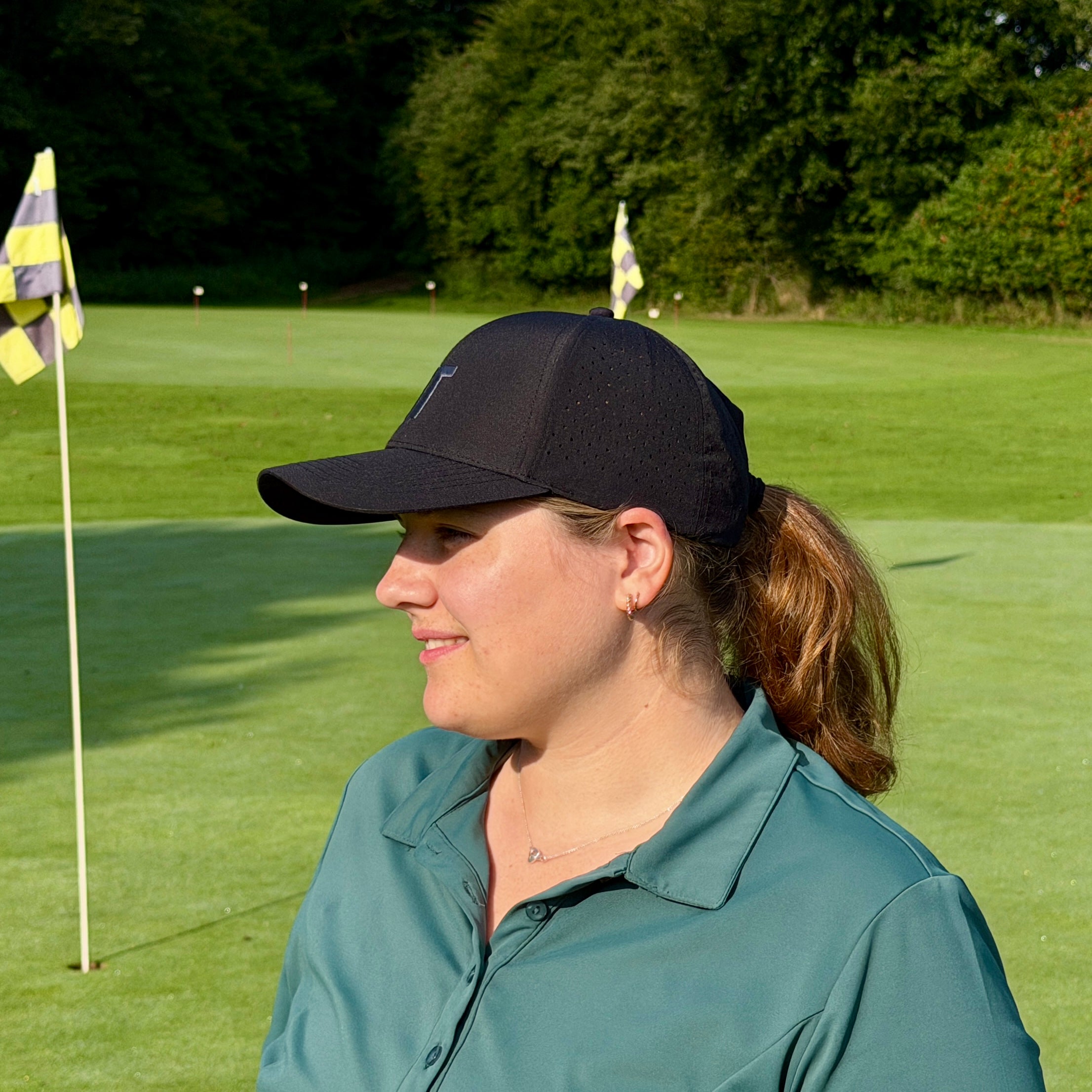 Person trägt THE CUTLINE Focus Cap in Schwarz auf dem Golfplatz, Seitenansicht