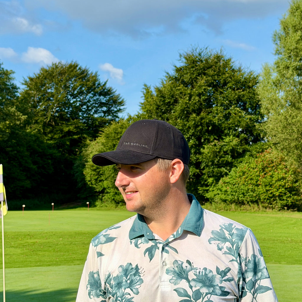 Person trägt THE CUTLINE Steady Cap in Schwarz mit dezentem Logo auf dem Golfplatz, Seitenansicht