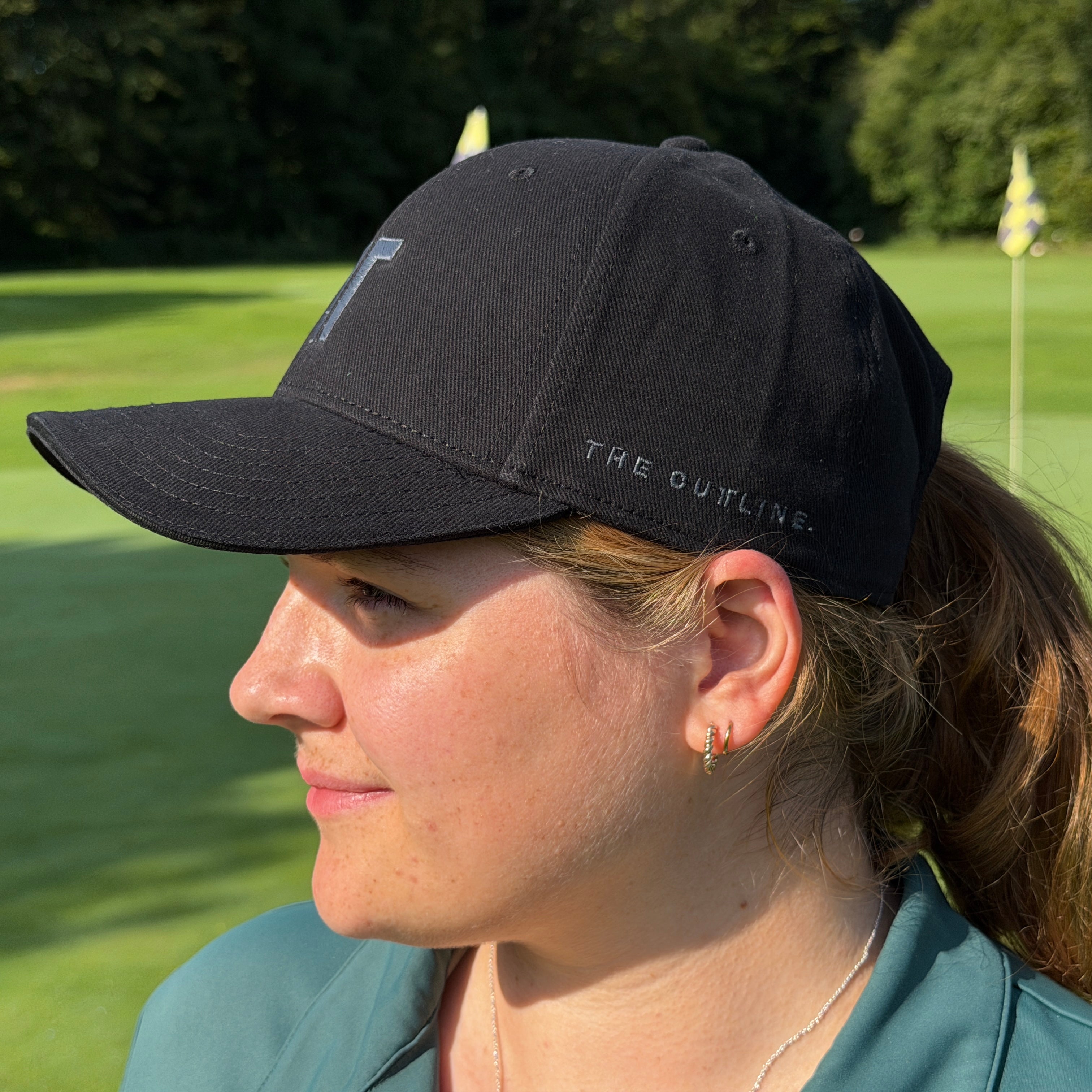 Person trägt THE CUTLINE Steady Cap in Schwarz auf dem Golfplatz, Seitenansicht