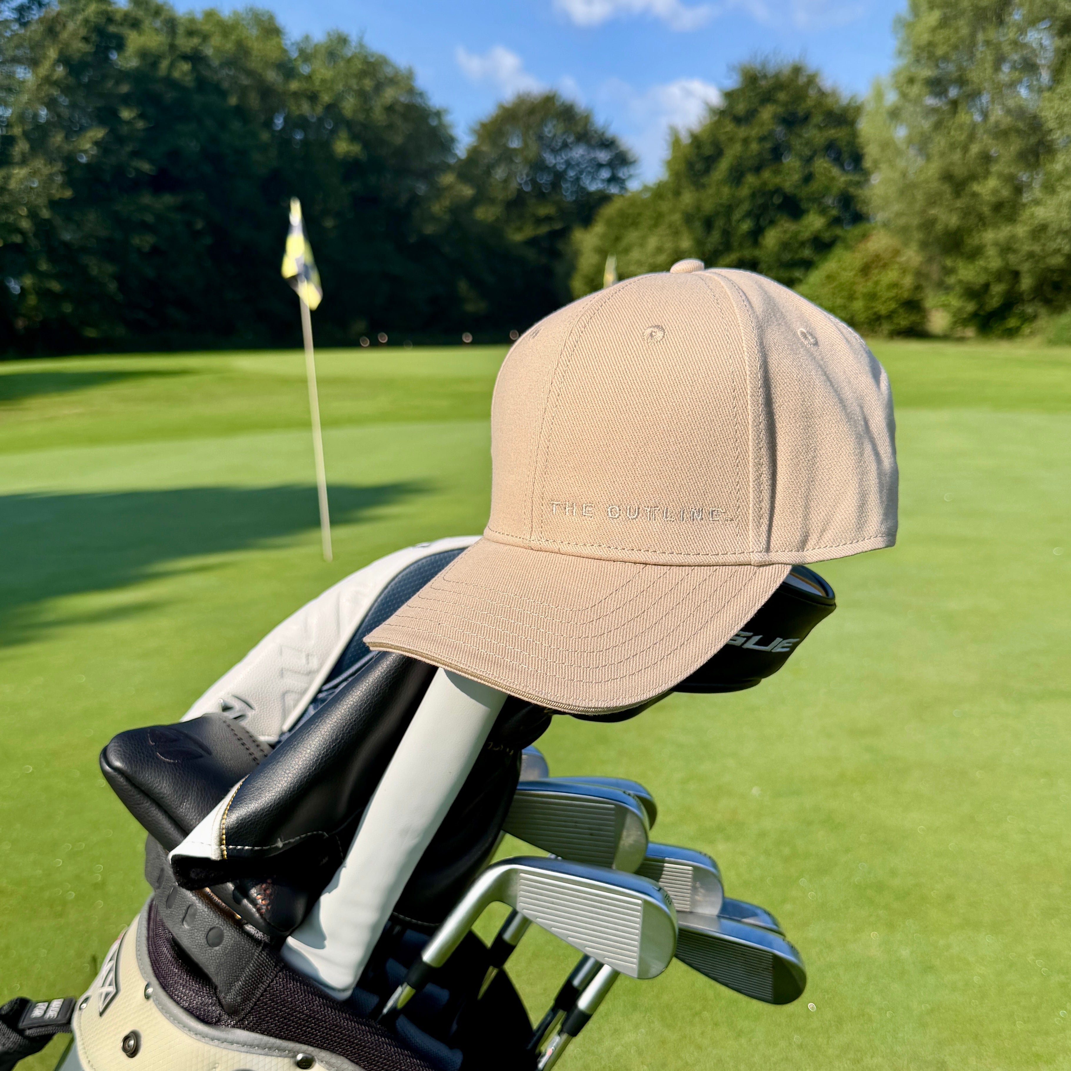 THE CUTLINE Steady Cap in Sand mit dezentem Logo hängt am Golfbag