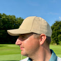 Person trägt THE CUTLINE Steady Cap in Sand auf dem Golfplatz, Seitenansicht