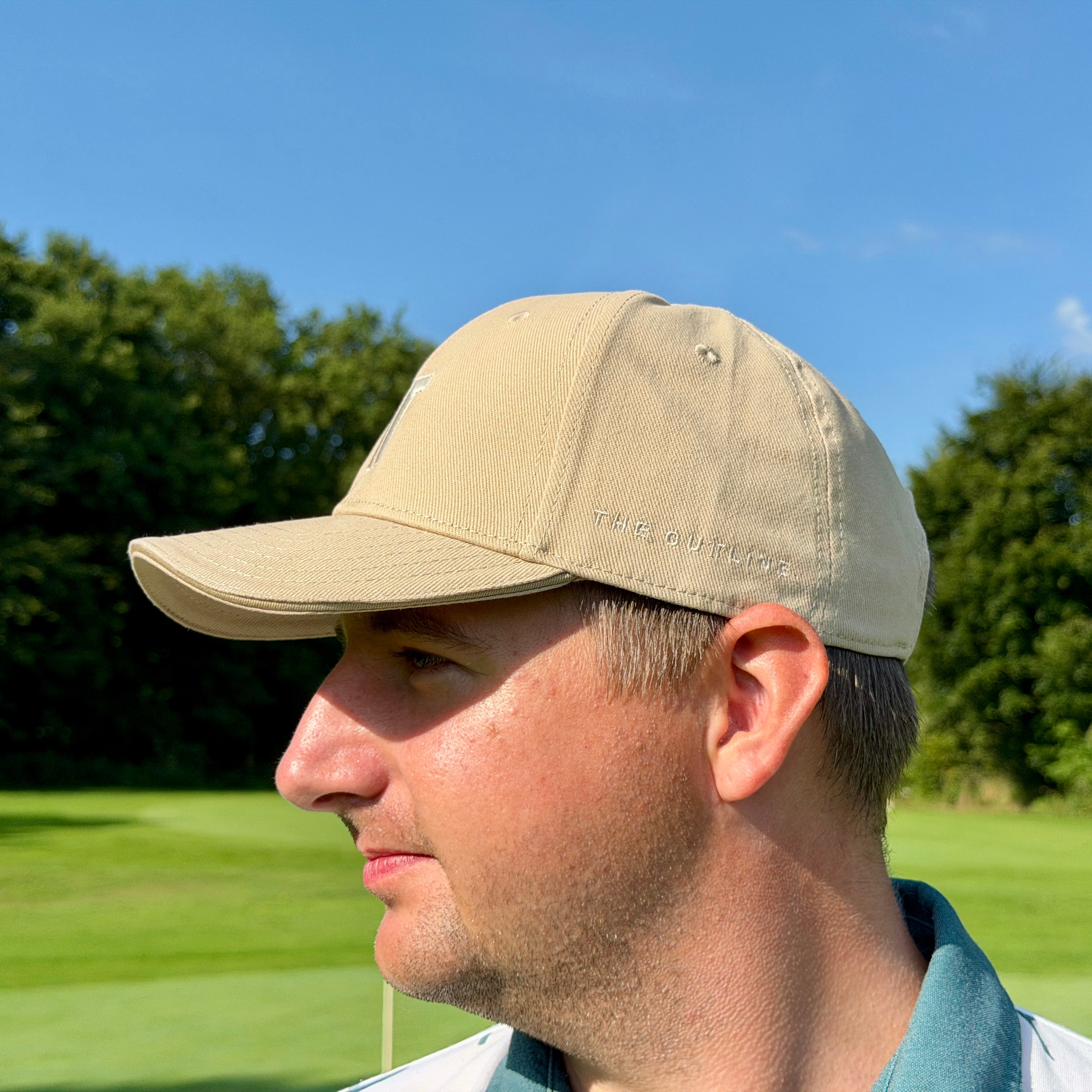 Person trägt THE CUTLINE Steady Cap in Sand auf dem Golfplatz, Seitenansicht